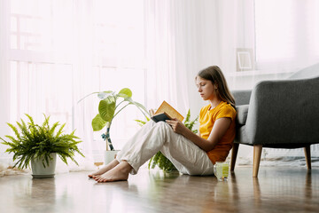 A young girl is sitting in a chair and exchanging messages online on her phone. Home recreation, modern lifestyle