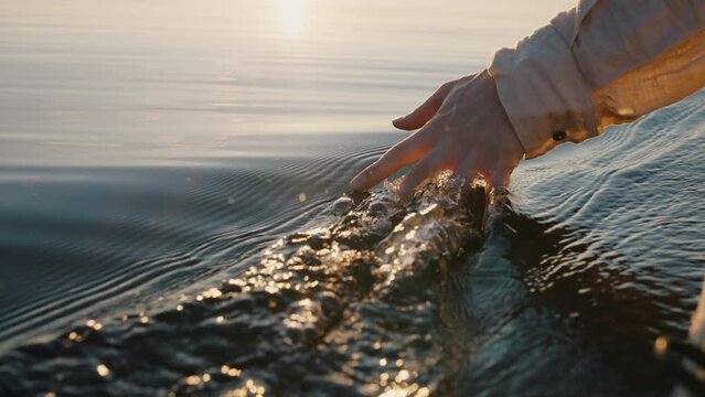 Person dips hand in calm river water sitting in yellow boat. Man enjoys camping and sailing on boat. Guy makes waves on water with hand