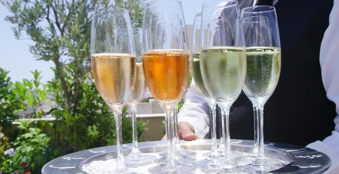 Waiter holds tray of sparking Champaign glasses of various flavors on patio
