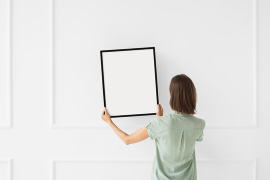 Woman hold blank picture frame mockup on white wall, Artwork mock-up in minimal interior design, Minimal photographer artist concept.