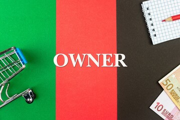 OWNER - word (text) and euro money on a table of different colors, a trolley, a basket of grocery notepad and a red pencil. Business concept, buying, selling, supermarket, store (copy space).