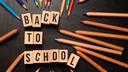 square wooden letters with the phrase "Back To School" written in English on a black chalkboard background and next to colored pencils