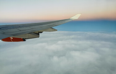 View from the porthole on the wing of an airplane with a red aircraft engine flying above beautiful white clouds.