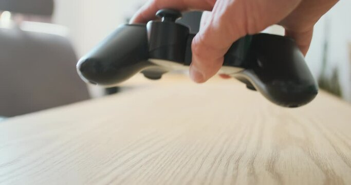 Hand raises the gamepad lying on the table. Side view, close-up.