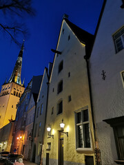 Naklejka premium Three brothers building complex and the St. Olaf Baptist Church on one of the streets of Old Tallinn against the dark blue sky. Spring evening.