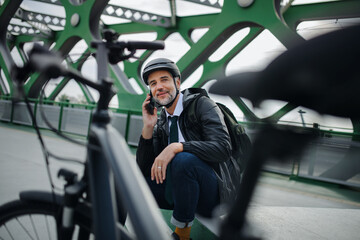 Businessman with bike sitting on bench, using smartphone. Commuting and alternative transport concept