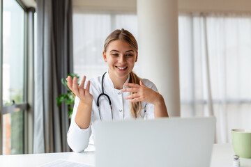 Attractive female doctor talking while explaining medical treatment to patient through a video call with laptop in the consultation.