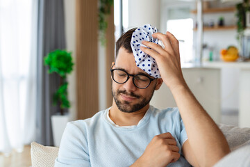 When you hit shelf with your head. Frustrated young man holding ice bag on his head while lying on the couch at home