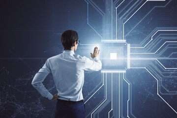 Back view of young businessman using creative glowing chip circuit hologram on dark background. CPU and metaverse concept.