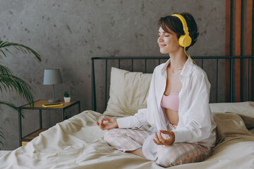 Young woman wear white shirt pajama headphones she lying in bed listen to music mantra meditating...