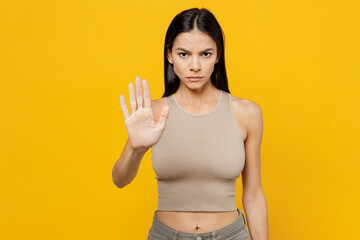 Young strict sad latin woman 30s she wearing basic beige tank shirt showing stop gesture with palm refusing reject say no isolated on plain yellow backround studio portrait. People lifestyle concept.