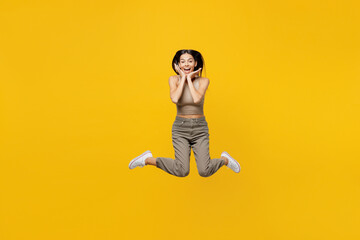 Fototapeta na wymiar Full body young overjoyed surprised excited fun cool latin woman 30s she wear basic beige tank shirt jump high hold face isolated on plain yellow backround studio portrait. People lifestyle concept.