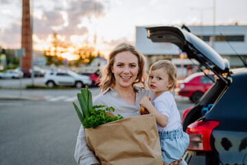 Young mother with little daughter after shopping holding zero waste shopping bags with grocery near...