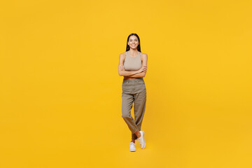 Fototapeta na wymiar Full body smiling happy fun young latin woman 30s she wear basic beige tank shirt looking camera hold hands crossed folded isolated on plain yellow backround studio portrait People lifestyle concept