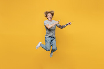 Full body young caucasian man 20s he wear grey t-shirt pointing index finger aside indicate on workspace area copy space mock up isolated on plain yellow backround studio. People lifestyle concept