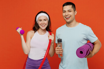 Young fitness trainer instructor sporty two man woman in headband t-shirt hold yoga mat hula hup bottle dumbbell spend weekend in home gym isolated on plain orange background. Workout sport concept.
