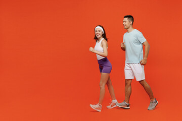 Fototapeta na wymiar Full body side view young fitness trainer instructor sporty two man woman in headband t-shirt jogging go spend weekend in home gym isolated on plain orange background. Workout sport lifestyle concept.