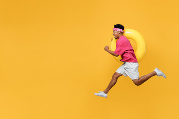 Fototapeta na wymiar Side view happy fun cool young man he wear pink t-shirt near hotel pool jump high run fast hurrying up hold inflatable rubber ring isolated on plain yellow background Summer vacation sea rest concept