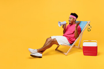 Full body young man he wearing pink t-shirt bandana lying on deckchair sunbad near hotel pool hold scream in megaphone announces isolated on plain yellow background. Summer vacation sea rest concept.