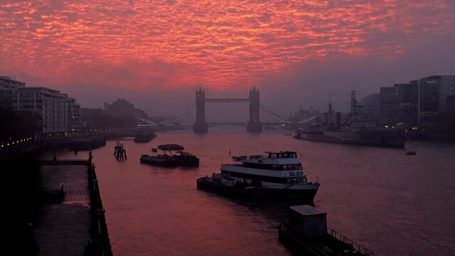 Vibrant, dramatic sunrise clouds and fog above Tower Bridge and the River Thames in London, England.  Zoom out.