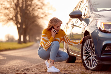 Woman Calling For Help On Phone After Car Breakdown On Country Road With Tyre Puncture