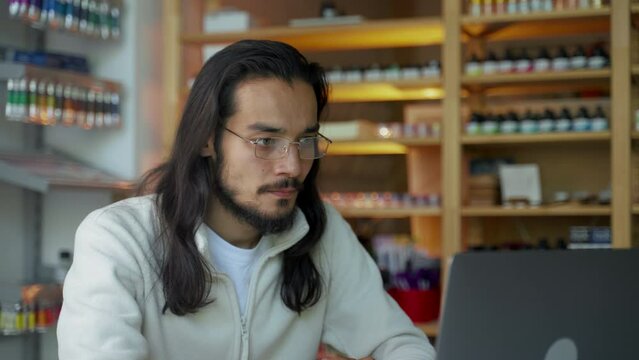 Concentrated brunet man in glasses takes part in online business conference looking at screen of laptop. Young manager sits at table in office closeup