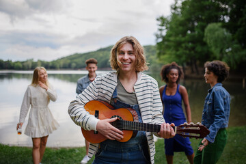Fototapeta premium A group of young friends having fun near a lake, laughing and playing guitar.