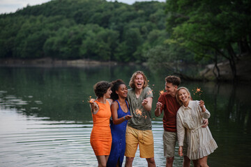 Happy group of friends lighting sparklers and enjoying freedom at beach during sunset