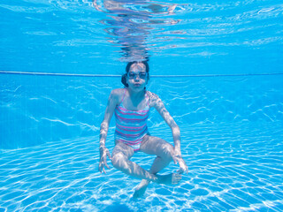 Brave girl breathing out air bubbles. Female with goggles relaxing underwater in the blue waters of...