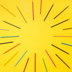 Coloured pencils like sun rays on yellow background. Minimal school and fun concept.