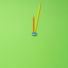 Two coloured pencils and blue sharpener on green background arranged in clock shape. Ready for...