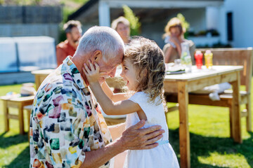 Happy little girl embracing her grandfather at generation family birthday party in summer garden.