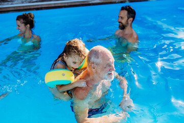 Multi generation family having fun and enjoying swimming in backyard pool during summer holiday.