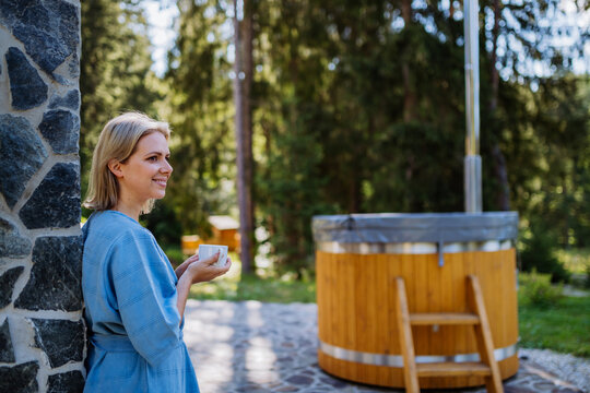 Happy Young Woman Standing In Garden Near Hot Tub And Enjoying Cup Of Morning Coffee On Summer Vacation In Mountains.