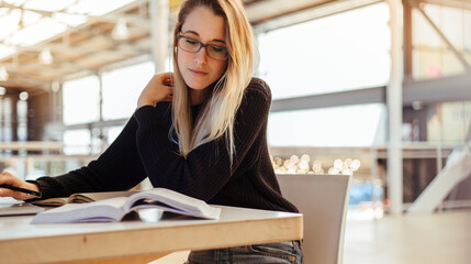 Young student with blond hair reading books in library
