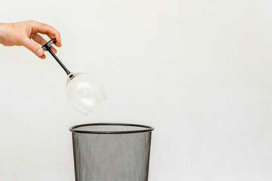 A glass of wine is thrown into the trash,can for disposal and recycling.White,gray background,selective focus,copy space.