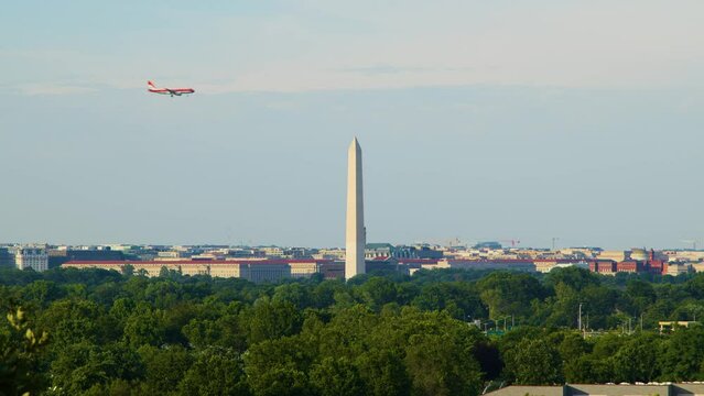 A commercial passenger jetliner airplane flies past the Washington, Monument in Washington, D.C. on its approach to Ronal Reagan National Airport in Arlington, Virginia. Seen on a summer evening.
