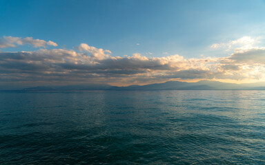 Fototapeta premium Cloudy sky above the sea and mountains in the horizon's background. The change of weather is continuous in all seasons. Calm, relaxing, scenic view.