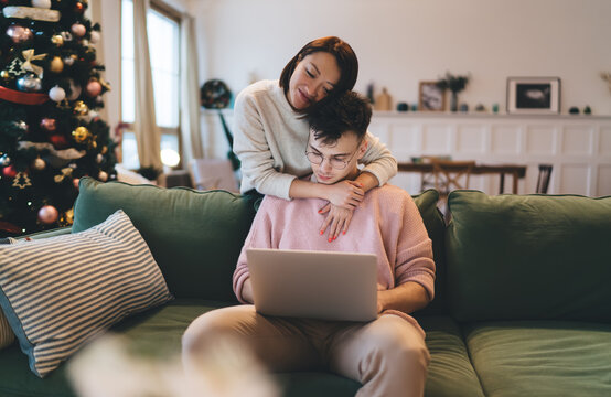 Asian woman hug caucasian man with laptop on sofa