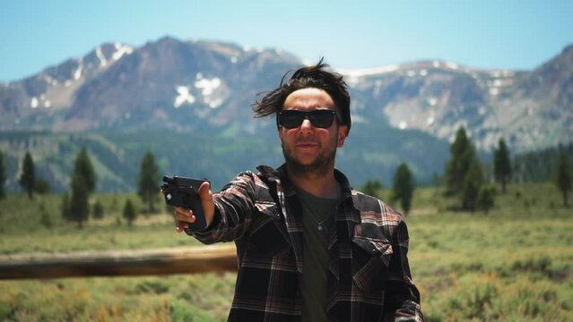 Caucasian gunman points handgun in a picturesque mountain range. fixing hair, gun fails
