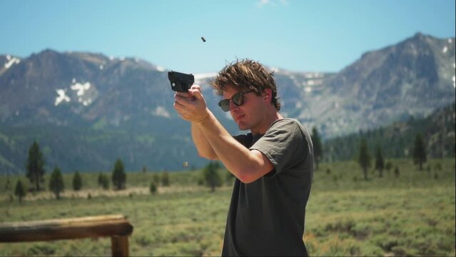 Young man aims and shoots 9mm handgun at picturesque target range, slow motion