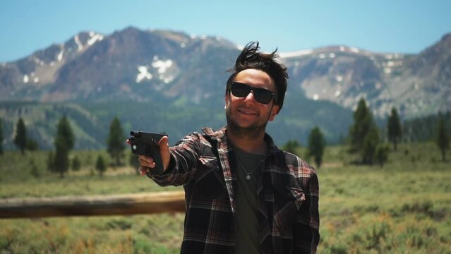 Caucasian man aiming a gun, smiling on mountainous background, slow motion