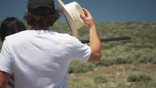 Couple having fun man puts hat on woman while skeet shooting with pump action shotgun