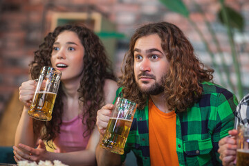 Happy couple together on the sofa at home watching on the tv a favourite sport match they getting excited and hugging each other when their team are winning