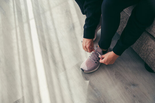 Low Section Of Woman Tying Sports Shoelace On Floor At Home