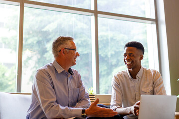 Smiling multiracial male partners discussing over laptop