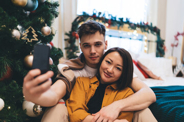 Couple take selfie on smartphone by christmas tree