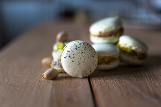 Homemade pistachio and chocolate macaroons stacked up on wooden table with pistachio nuts