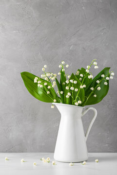 Still life with lily of the valley flowers bouquet in vase on gray concrete background. Vertical orientation