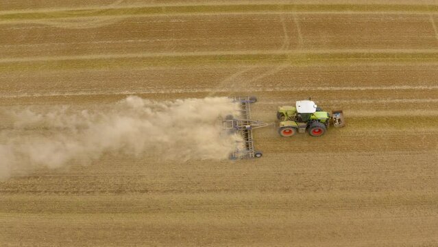 Tractor plowing field. Aerial view of moving tractor with plow raising dust.  Tractor plows ground on cultivated farm field. Farmer with tractor tilling the field to open the soil. 